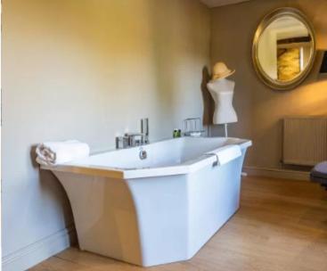 a large white tub in a bathroom with a mirror at Bagshaw Hall in Bakewell