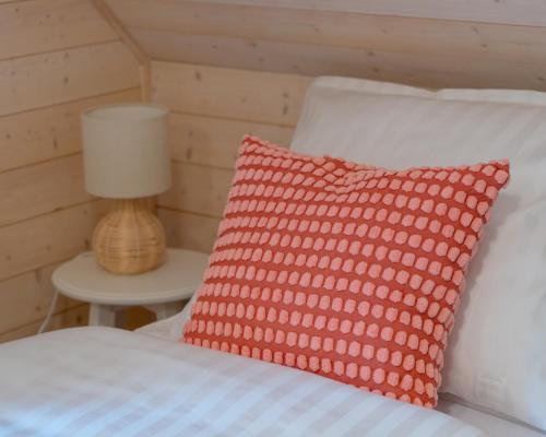 a bed with a red pillow and a lamp on a table at Siedlisko Modrej Czapli. Domki na Kaszubach in Klonowo Dolne