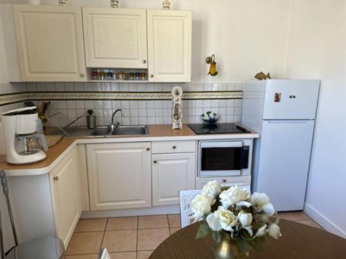 a kitchen with white cabinets and a table with a vase of flowers at Charmant T2 saint Enogat in Dinard