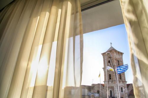 a building with a clock tower behind a window at Hotel Opera in Larnaca