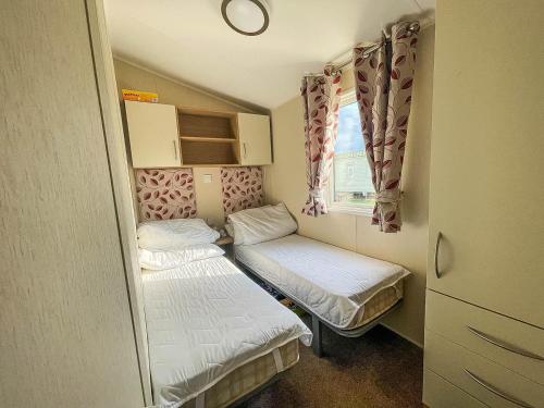 Habitación pequeña con 2 camas y ventana en Caravan With Decking And Free Wifi At Seawick Holiday Park Ref 27214sw, en Clacton-on-Sea