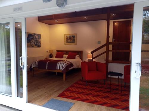 a bedroom with a bed and a red chair at Lamorna Pottery B&B in Penzance
