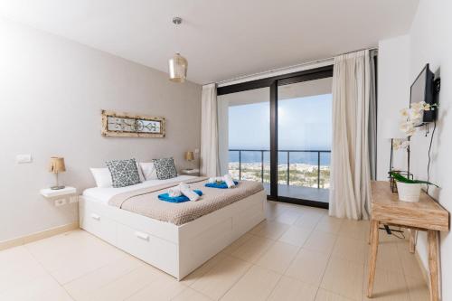 a white bedroom with a bed and a large window at Sunset White Villa - Ocean view, sunset,pool,grill in Playa de las Americas