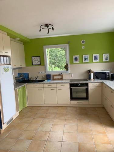 a kitchen with green walls and white cabinets and a window at Maison 400m de la plage in Crozon