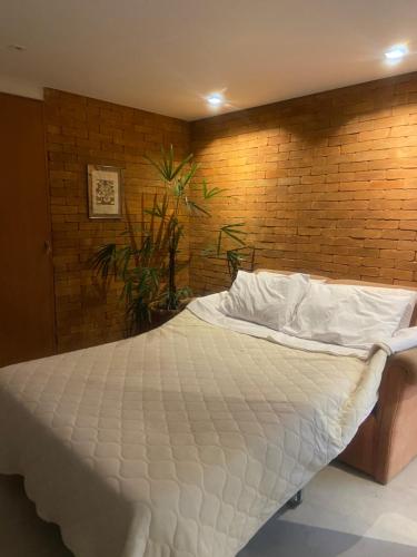 a bedroom with a white bed with a brick wall at Loft da Beth na serra in Petrópolis