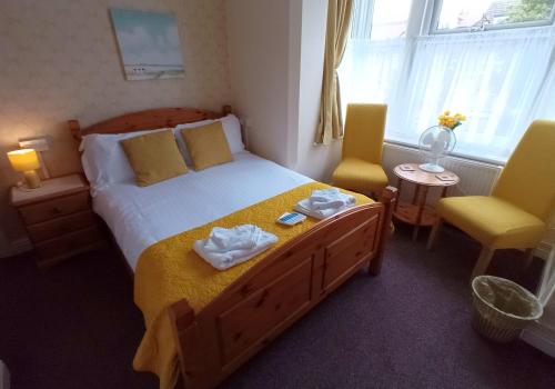 a bedroom with a large bed with two yellow chairs at Brackenhurst Guest House in Skegness