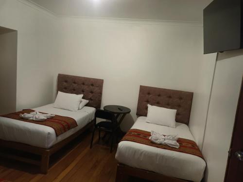 two beds in a room with a table and a stool at Paqarina San Blas in Cusco