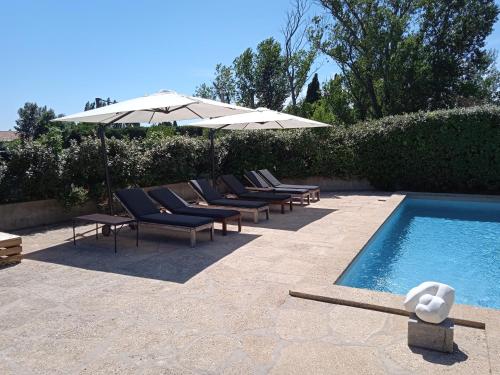 a row of lounge chairs and an umbrella next to a pool at Mazet Des Artistes in Mouriès
