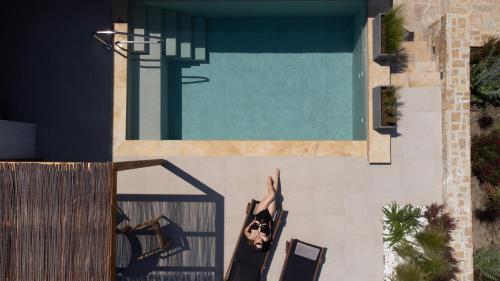 a woman sitting in a chair next to a swimming pool at Pnoes Luxury Suites in Paliouri