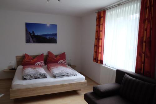 Schlafzimmer mit einem Bett mit roten Kissen und einem Fenster in der Unterkunft Putz Appartements in Gröbming