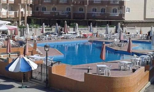 een groot zwembad met parasols en tafels en stoelen bij شاليه قريه عايدة -مصر الجديده- عائلات فقط in El Alamein