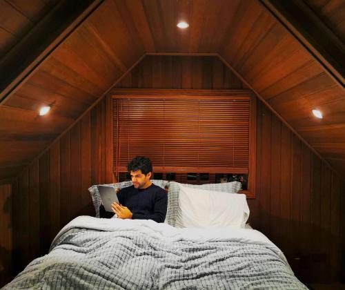 Ein Mann, der auf einem Bett auf einer Tafel sitzt in der Unterkunft Mansão Austríaca Guesthouse in Campos do Jordão