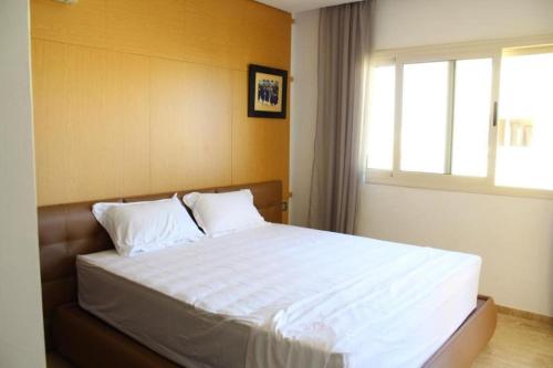 um quarto com uma cama com lençóis brancos e uma janela em Appt 22 Bloc G- Hicherraton plage Residence Bella Vista, BOUZNIKA BAY em Skhirat