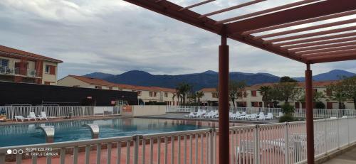 a swimming pool with white chairs and mountains in the background at VILLA 6 à 8 personnes dans résidence de tourisme in Argelès-sur-Mer