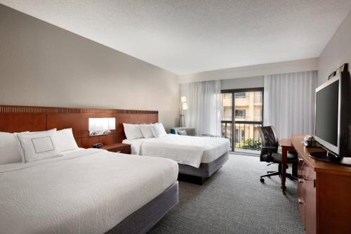 a hotel room with two beds and a flat screen tv at Courtyard Fort Myers Cape Coral in Fort Myers