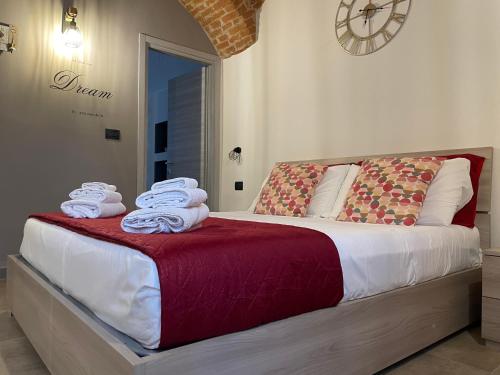 a bed with towels on it with a clock on the wall at HappyHome Bilocale centro storico Rivarolo Canavese in Rivarolo Canavese