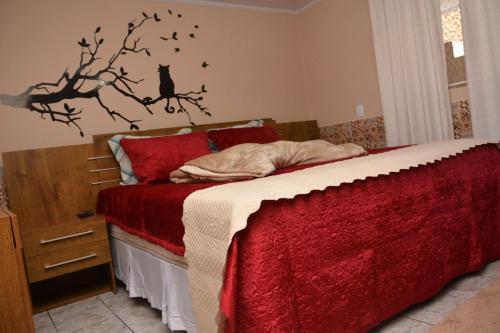 a bedroom with a bed with a red blanket and a black cat on a tree at Cantinho Bebler in Santa Teresa
