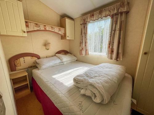 a small bed in a small room with a window at Brilliant Caravan With Decking And Wifi At Dovercourt Park In Essex Ref 44010a in Great Oakley