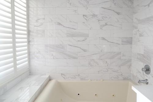 a white bath tub in a bathroom with white tiles at Days Inn by Wyndham Near City Of Hope in Duarte