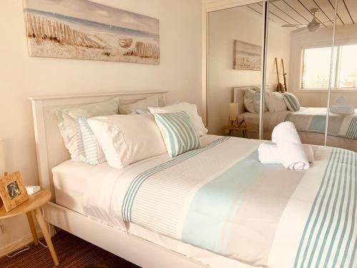 a white bed with white pillows and a mirror at Cooly Coastal Escape walk to beach & shops in Gold Coast