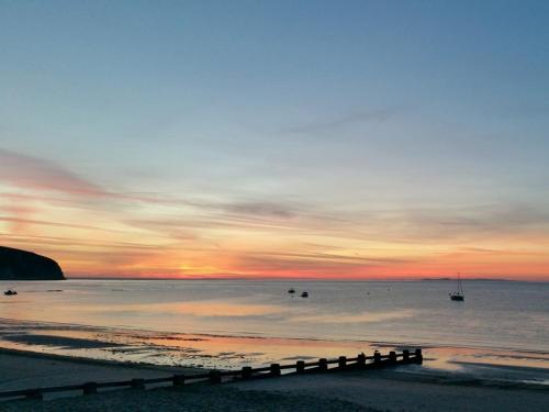 a sunset over a beach with boats in the water at Beachcomber Holiday Apartments in Swanage