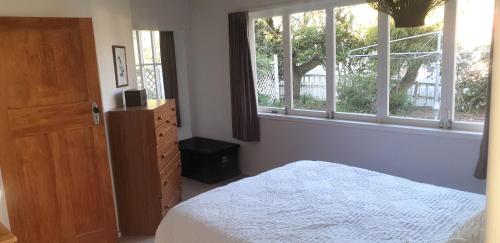 a bedroom with a bed and a dresser and windows at Pohutukawa Villa 