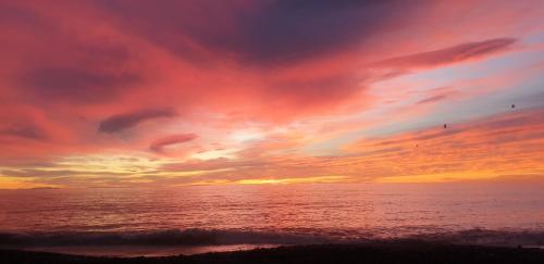 a sunset on the beach with the ocean at Pohutukawa Villa in Waipureko