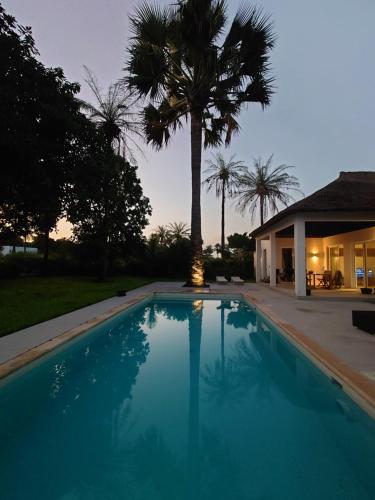 a swimming pool in front of a house with a palm tree at Villa Cap Ouest Piscine Grand Jardin à 2 Pas de l'Océan in Cap Skirring