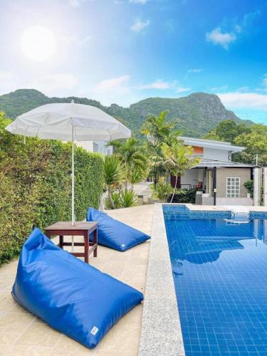 a swimming pool with blue pillows and an umbrella at พูลสวัสดิ์ รีสอร์ท อ่าวมะนาว in Changwat Prachuap Khiri Khan