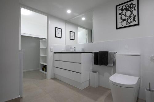 a white bathroom with a toilet and a sink at Resort Living, Luxury Getaway, Close 2 Noosa River in Noosaville