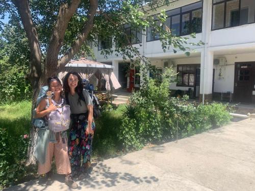 two women standing next to a tree in front of a building at Salom Hostel in Panjakent