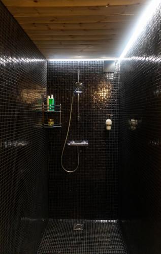 a black tiled bathroom with a shower and a sink at Pirtis pas Astą in Lelaičiai