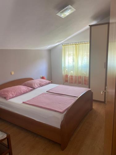 Schlafzimmer mit einem Bett mit rosa Bettwäsche und einem Fenster in der Unterkunft Apartments Nautica in Barbat na Rabu