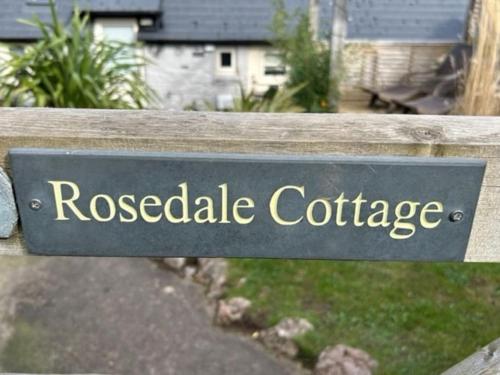 um sinal num banco de madeira que lê café de Rosedale em Rosedale a charming detached 4 bedroom cottage. em Brixham