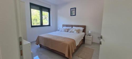 a white bedroom with a bed and a window at Apartmani Mariosa in Vrbnik