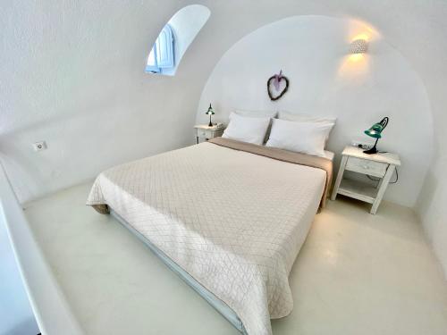 a white bedroom with a bed and a window at Heliades Apartments in Imerovigli