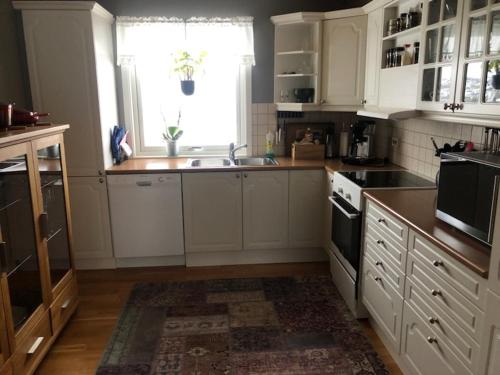 cocina con armarios blancos, fregadero y ventana en Sentral og hyggelig bolig en Svolvær