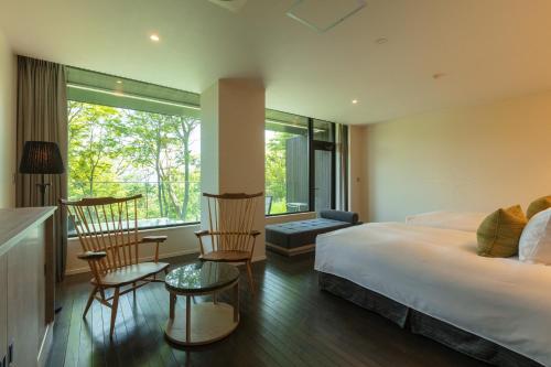 a bedroom with a bed and chairs and a window at KANAYA RESORT HAKONE in Hakone