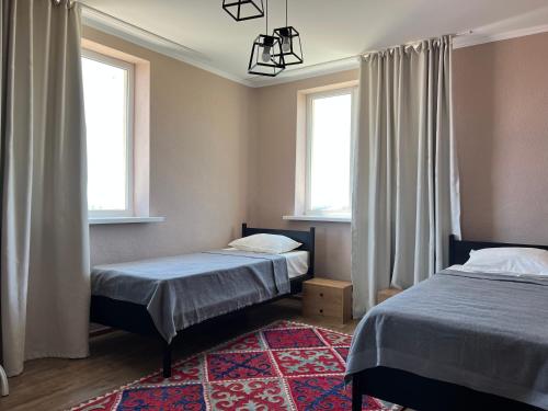 two beds in a room with two windows and a rug at Guest house Hygge in Cholpon-Ata