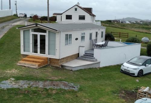 una pequeña casa blanca con un coche aparcado al lado en Cascade Lodge & Hot Tub F94 H0FR, en Donegal