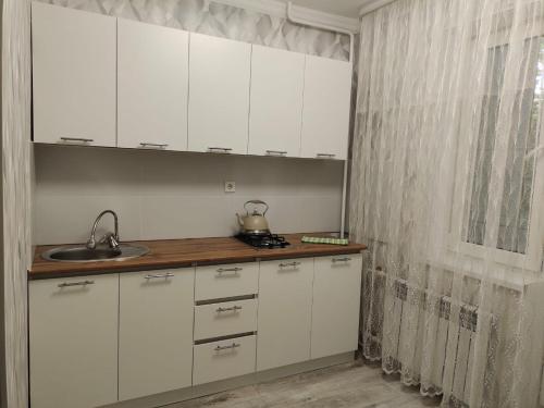 una cucina con mobili bianchi, un lavandino e una finestra di Квартира в городе Хромтау a Khromtaū