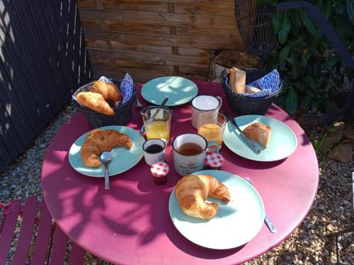 una mesa rosa con platos de repostería y vasos de zumo de naranja en Studio de Jardin "Le Temps d une Pause" jusqu'à 4 personnes en face du Beaujolais - Climatisation et Borne recharge véhicule électrique, en Montmerle Sur Saône