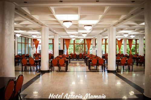 un gran salón con sillas, mesas y ventanas en Hotel Astoria en Mamaia