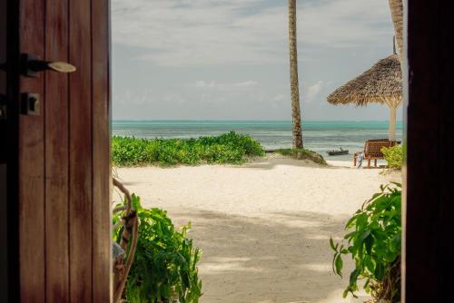 an open door to a beach with an umbrella and chairs at Savera Beach Houses in Jambiani