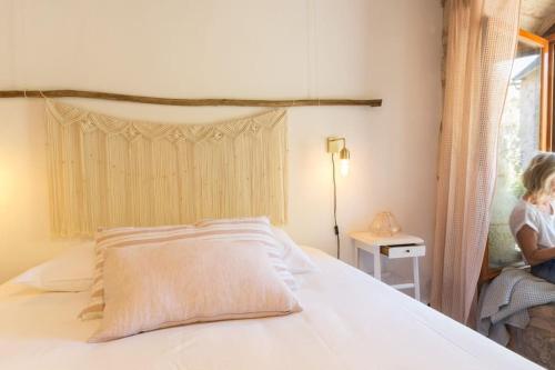 une femme assise sur un lit à côté d'une fenêtre dans l'établissement Maison Bons Jours. Grange traditionelle avec piscine, à Perpezac-le-Blanc