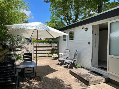 a patio with a table and an umbrella and chairs at Zomerhuis Duinzicht in Egmond aan den Hoef