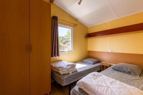 dwa łóżka w pokoju z oknem w obiekcie Camping des Templiers w mieście Le Caylar