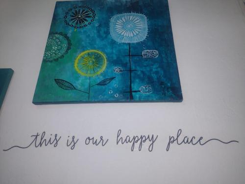 a painting hanging on a wall with the words this is our happy place at Casa Jardim Hostel BH - Santa Efigênia - Paraíso in Belo Horizonte