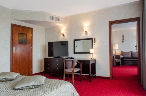 a hotel room with two beds and a desk with a television at Hotel Lidia Spa & Wellness in Darłówko