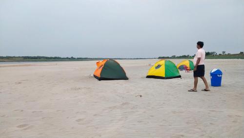 a man walking on a beach with three tents at Jhoomke camping and water sports adventure in Auraiya